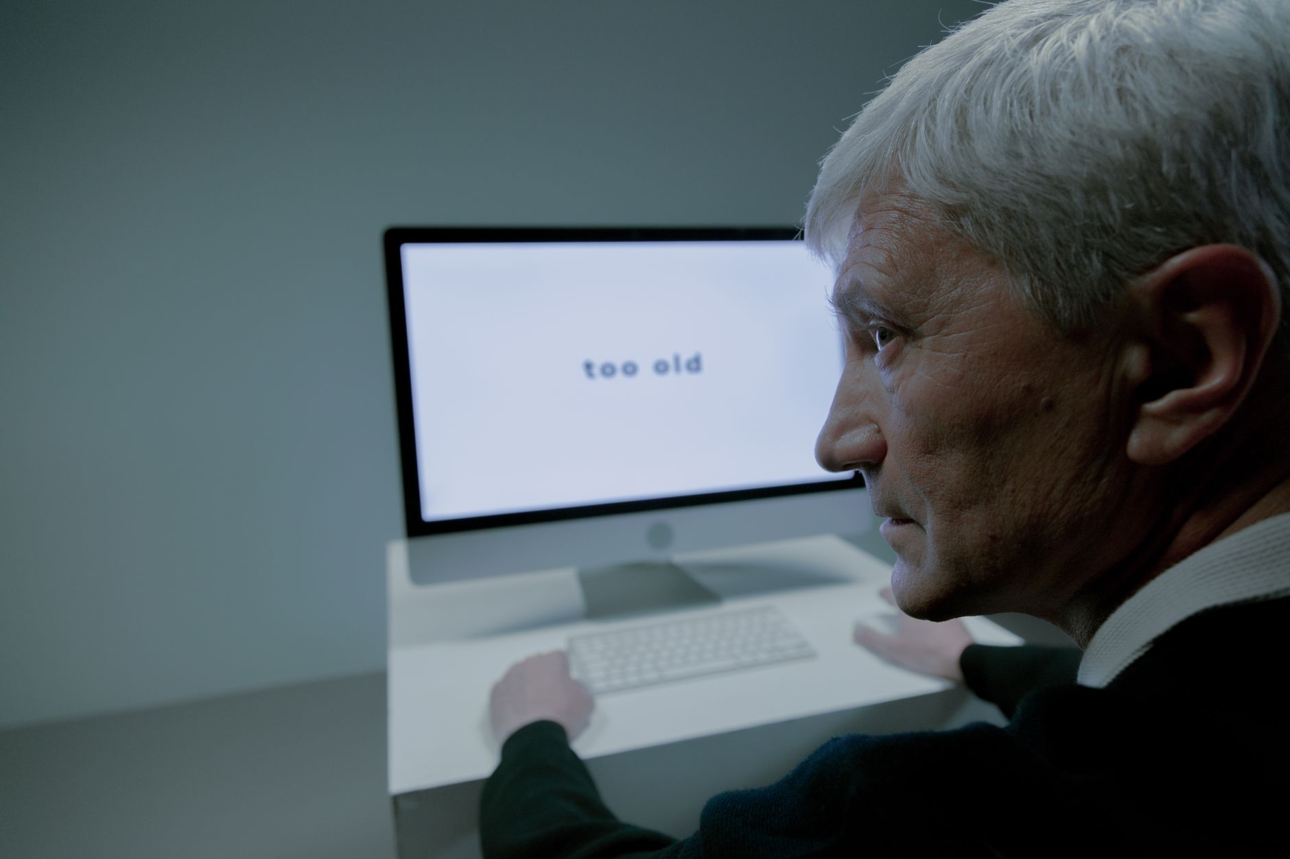 Senior man confronted with ageism on computer screen in job search.