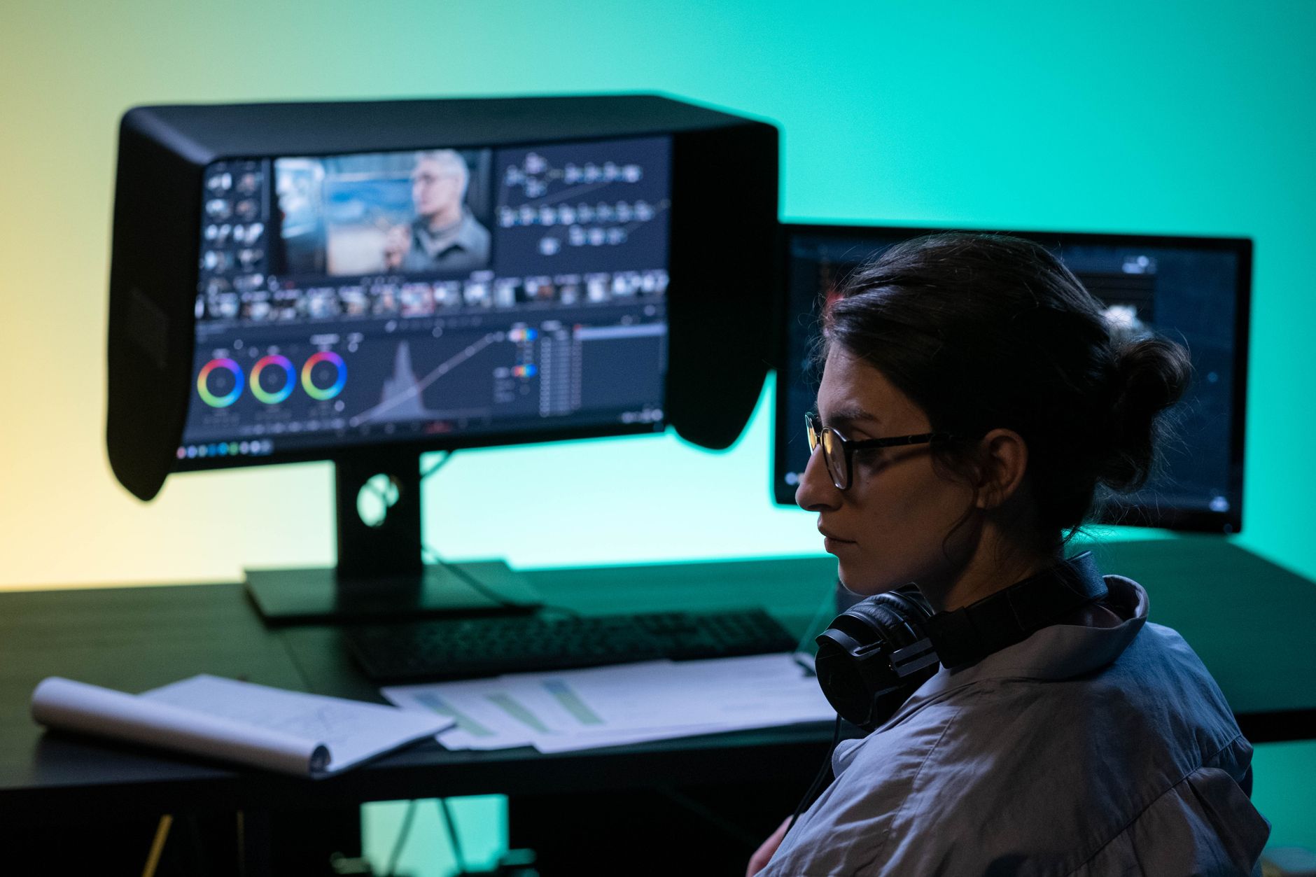 Focused video editor working at a dual-screen setup with colorful lighting ambiance.