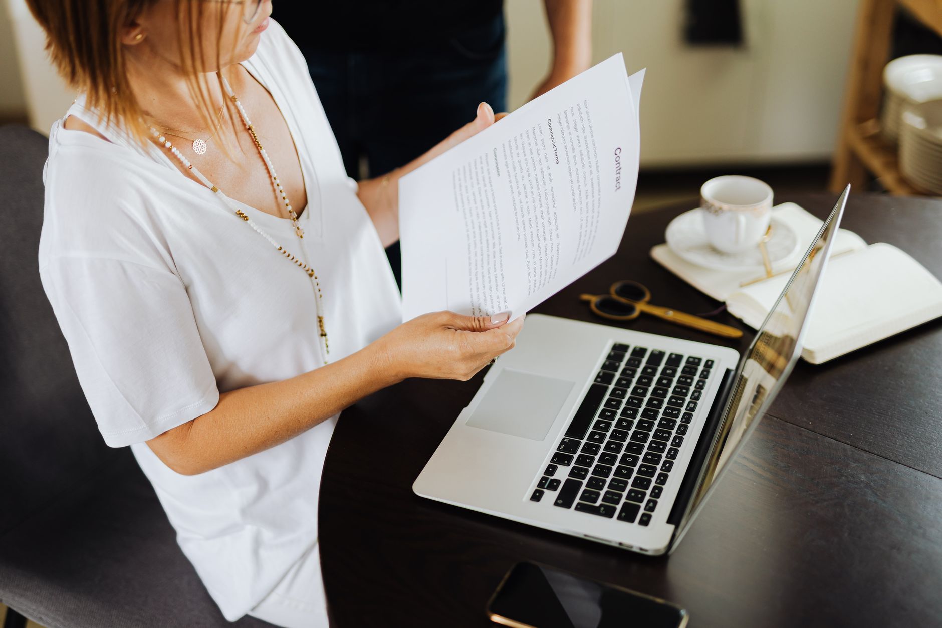 Businesswoman reviewing important documents at her desk with a laptop in a modern office setting.