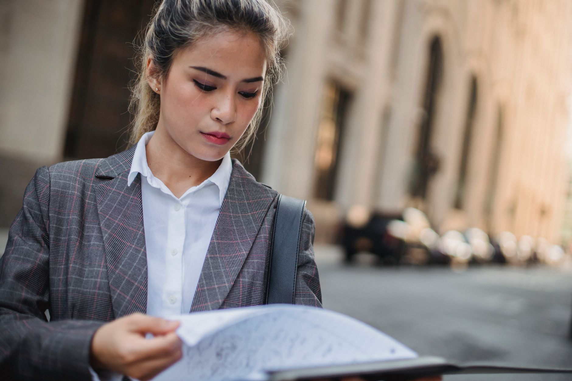 Businesswoman in corporate attire reviewing documents on a city street during the day.