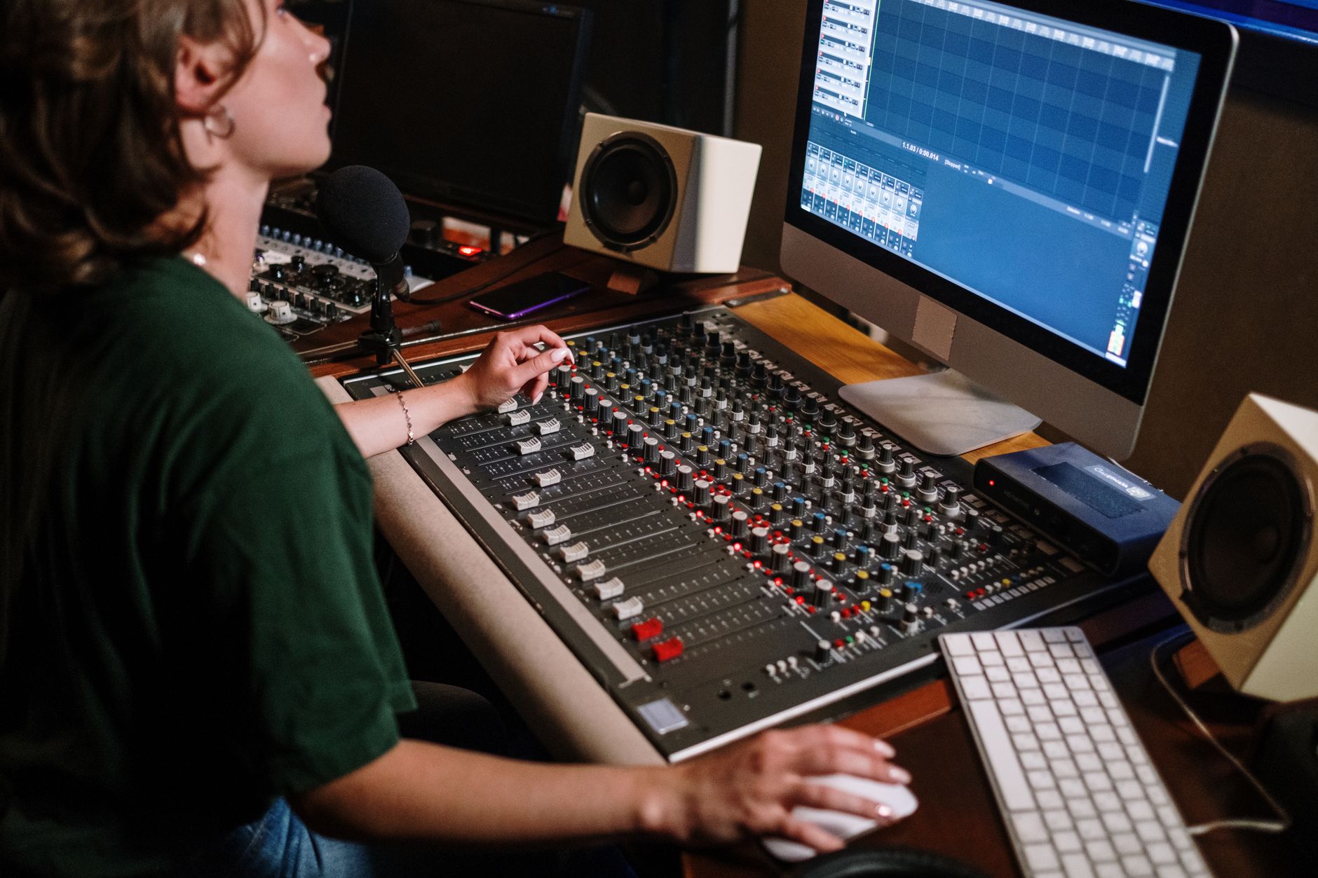 A sound engineer adjusting audio levels at a mixer desk in a recording studio with high-tech equipment.