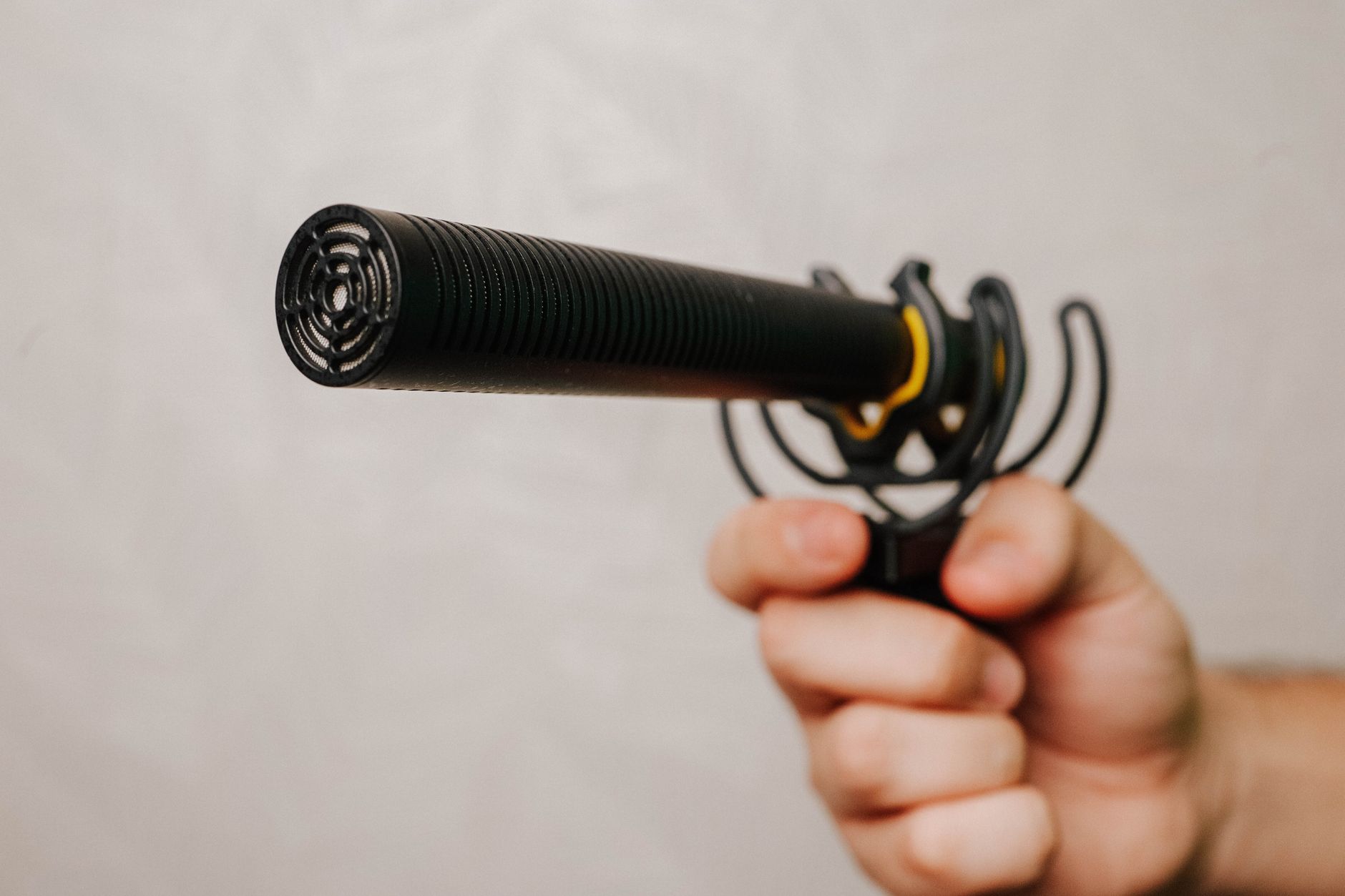 Hand holding a shotgun microphone with foam cover, ideal for voice recording and audio capture.